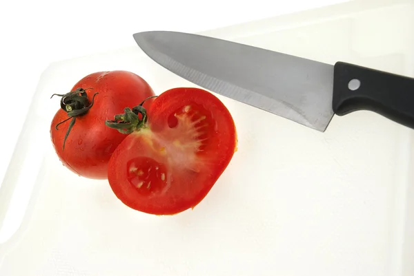 Corte de placa de plástico branco com uma faca e tomate — Fotografia de Stock