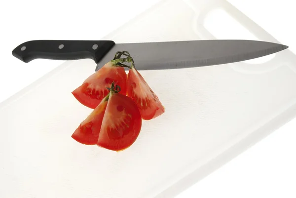 Резка белой пластиковой доски ножом и помидорами — стоковое фото
