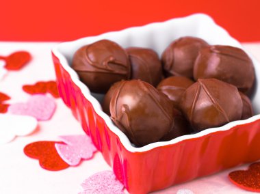 A delicious image of chocolates in a red dish with festive hearts scattered around clipart