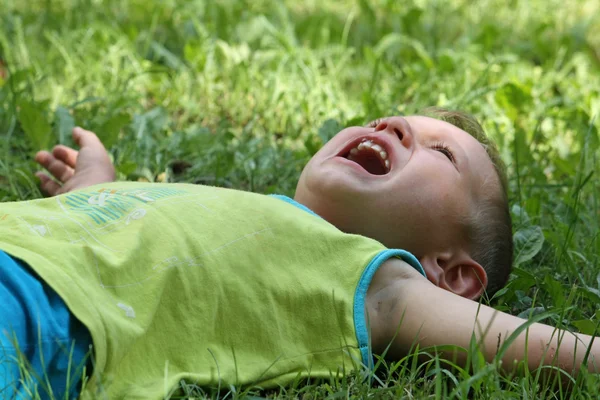 Der kleine Junge weint im Gras liegend — Stockfoto