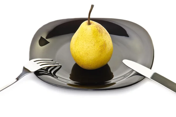 Yellow pear on a black plate with fork and knife — Stock Photo, Image