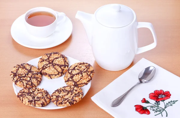 Biscuits with chocolate and peanut decoration, teapot and a cup of tea — Stock Photo, Image