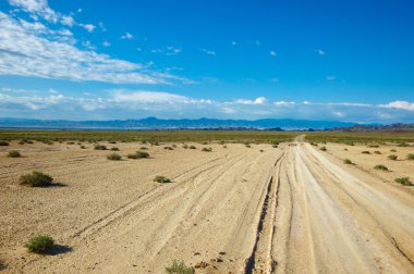 Dry road through steppe in far mountains in bright day clipart