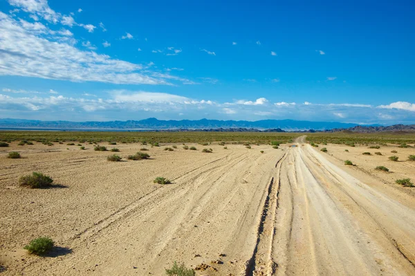 stock image Dry road through steppe in far mountains in bright day