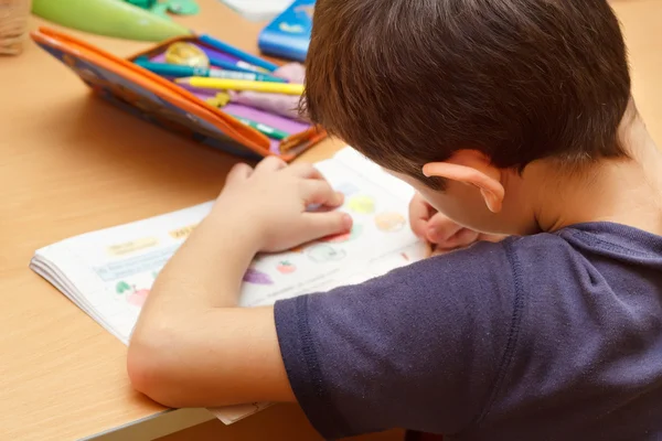 Menino fazendo lição de casa com lápis de cor, pintando frutas — Fotografia de Stock