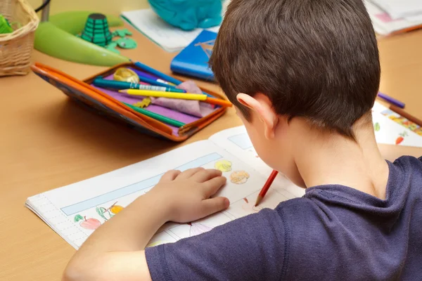 Мальчик делает домашнее задание цветным карандашом, рисует фрукты — стоковое фото