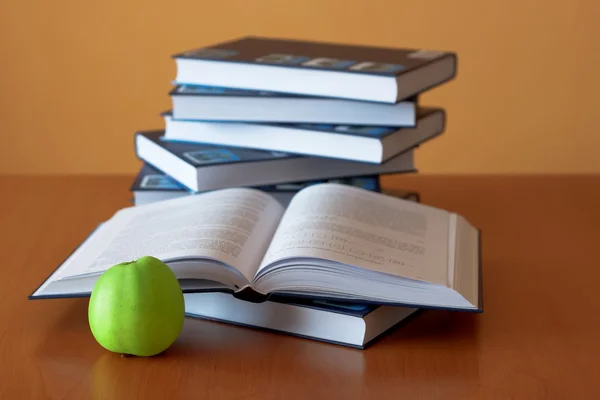 Зеленое яблоко и открытые книги на столе — стоковое фото