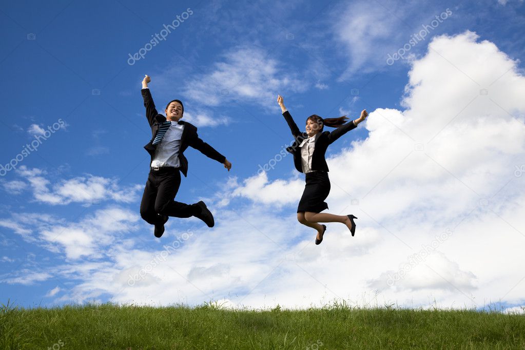 Businessman and businesswoman jumping on a green meadow