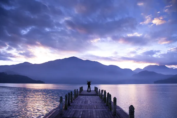 Человек стоит на пирсе и смотрит на горы и озеро — стоковое фото