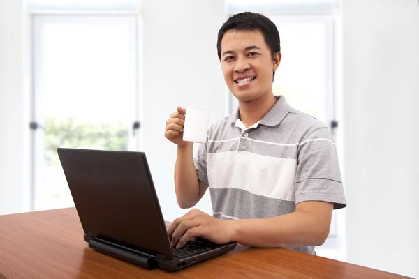 A happy young man holding a cup and using the latop — Stock Photo, Image