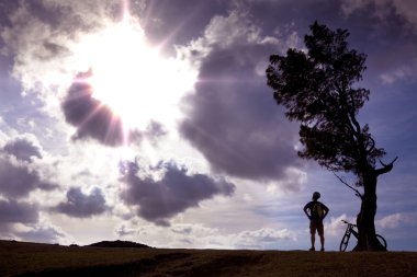 Bicycle rider stand on the hill watching the sunlight and relax clipart