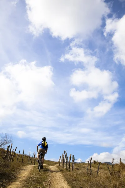 Jovem montando bicicleta de montanha e assistindo céu nublado — Fotografia de Stock