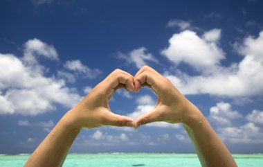 Hand forming a heart on tropical beach background clipart