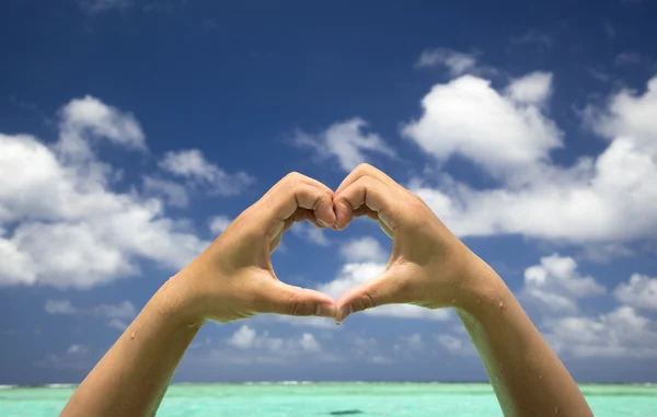 Рука формує серце на фоні тропічного пляжу — стокове фото