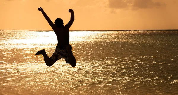 Счастливый молодой человек прыгает на пляже на закате — стоковое фото