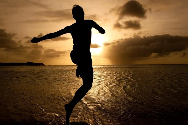 Silhouette eines Jungen, der bei Sonnenuntergang zum Meer springt — Stockfoto