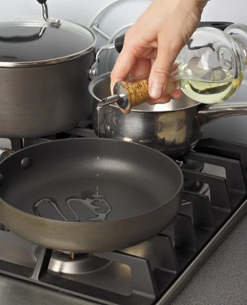 stock image Cooking oil being pourred from a glass bottle into a frying-pan.