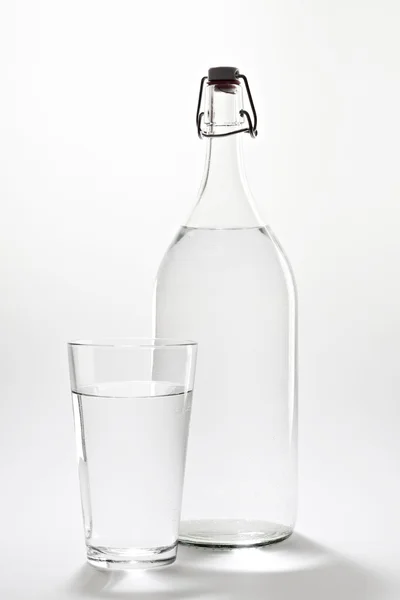 Transparante fles en glas met water. Stockafbeelding