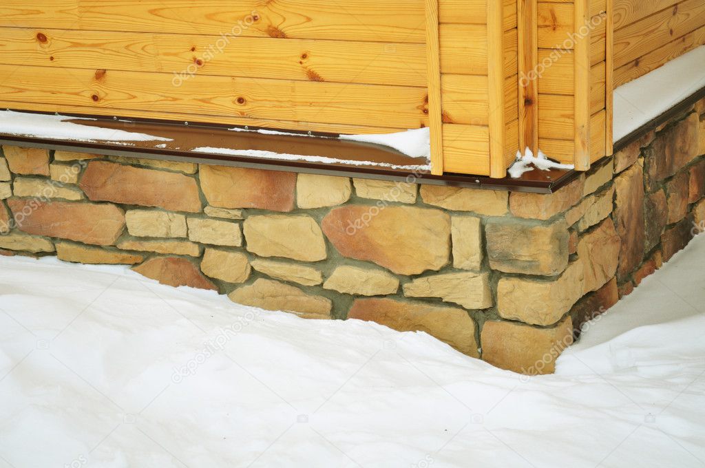 Stone, wooden wall of stained wood, cottage or chalet, corner constuction, basement exterior, winter photography, snow