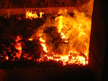 Fire in the coal boiler grate visible through an open manhole clipart