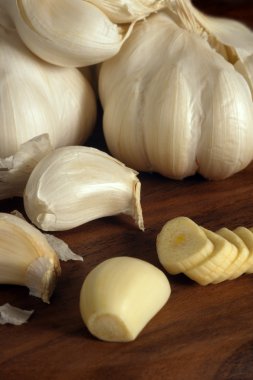 Cloves and sliced garlic on a wood cutting board. clipart