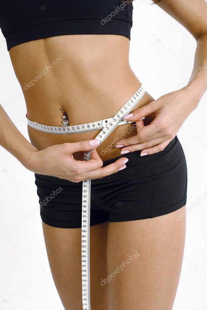 A tanned slim young woman measuring her waistline.