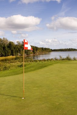 Red flag on the golf green at the water's edge clipart