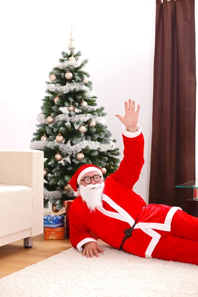 Санта-Клаус лежит на полу перед елкой — стоковое фото