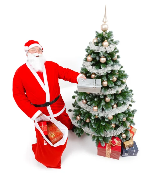 Санта Клаус предлагает подарок перед елкой — стоковое фото