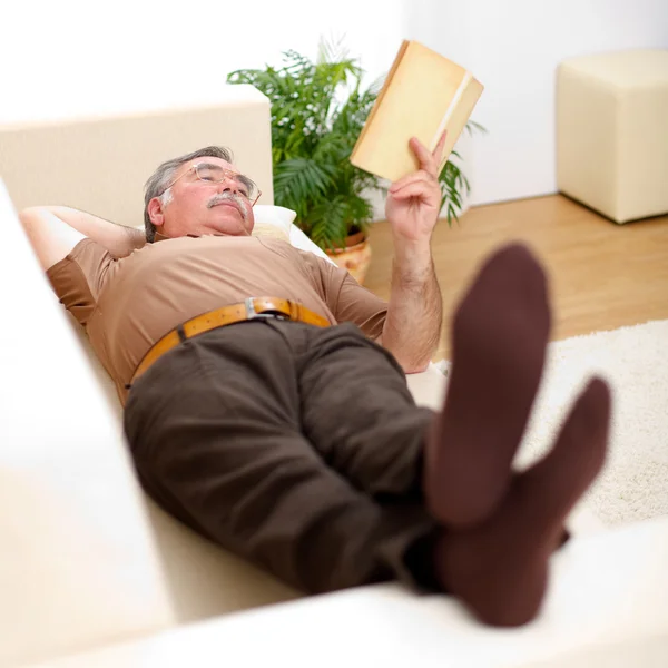 Senior man reading on sofa — Stock Photo, Image