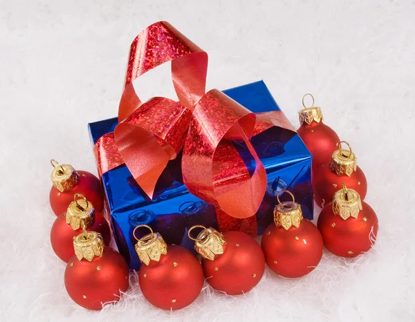 Red spheres and blue box with red bow on the white fur — Stock Photo, Image