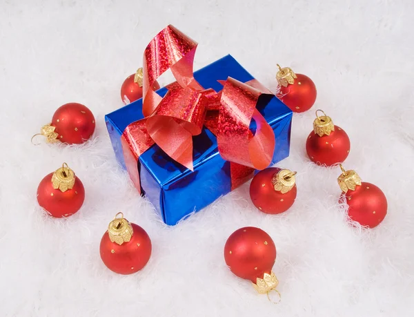 Blue box with red bow and red spheres on the white fur — Stock Photo, Image