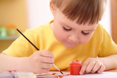 Child draws with paints in preschool clipart