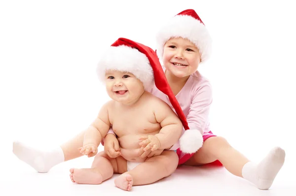 Zwei Kinder tragen rote Weihnachtsmützen und lächeln — Stockfoto