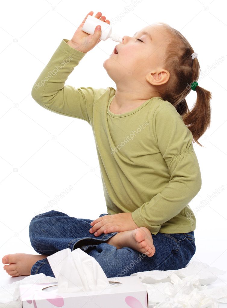 Little girl spraying her nose with nasal spray while sitting on floor, isolated over white