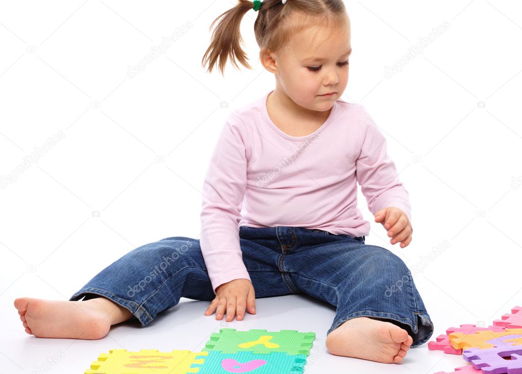 Cute little girl is playing with alphabet while sitting on floor, isolated over white