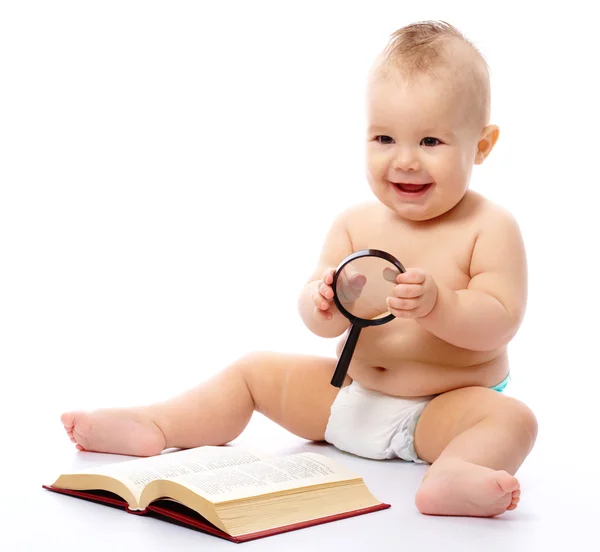 Niño pequeño juega con el libro y la lupa —  Fotos de Stock