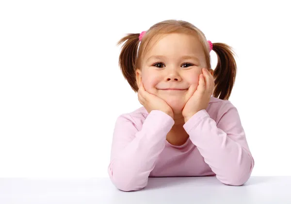 Счастливая маленькая девочка сидит за столом и улыбается — стоковое фото