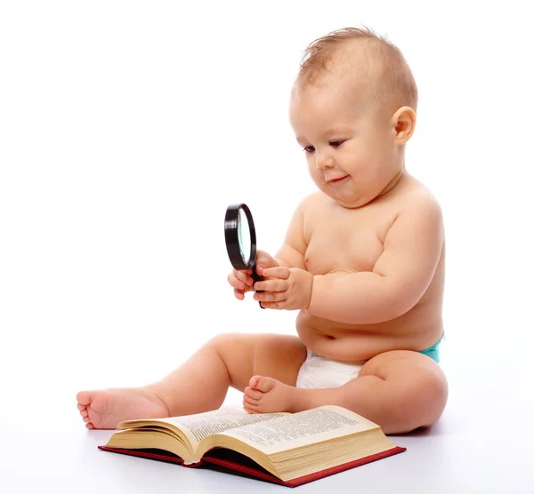 Маленький ребенок играет с книгой и лупой — стоковое фото