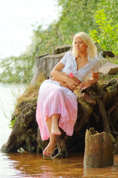 Молодая задумчивая женщина, сидящая на берегу реки или озера — стоковое фото