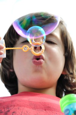 Küçük çocuk sabun köpüğü üflüyor.