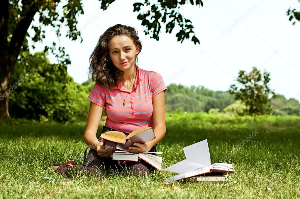 The girl sitting on a grass, reading a book