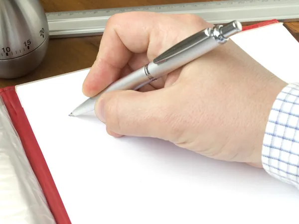 Hand holding a pen and sheet of a paper laying on a desk — Stock Photo, Image