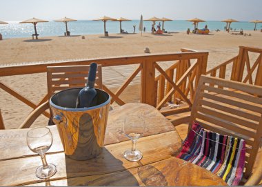 Wine bottle and glasses on a table at a beach clipart