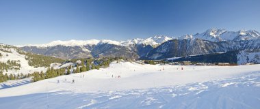 Panoramic view over a piste at ski resort with mountains in background clipart