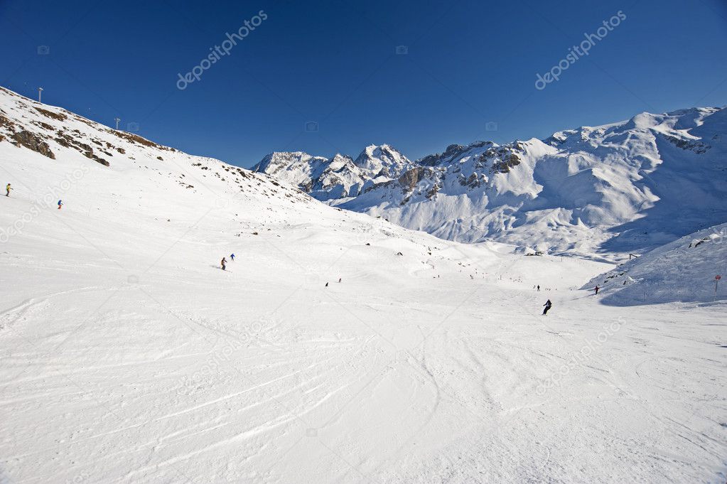 View down a piste with skiers and mountains