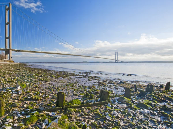 Large Suspension Bridge Spanning Wide River Rocky Beach Foreground — Stock Photo, Image