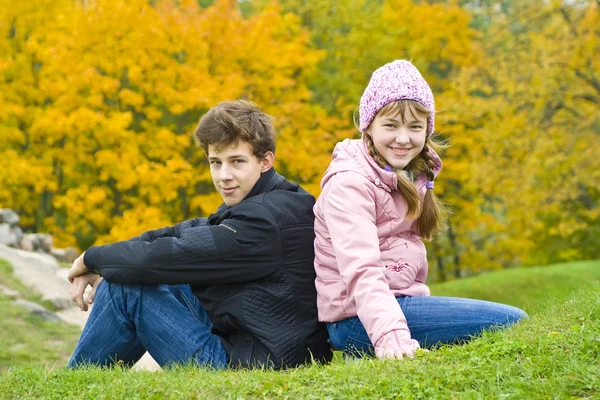 Irmão com irmã sentar-se contra folhas amarelas — Fotografia de Stock