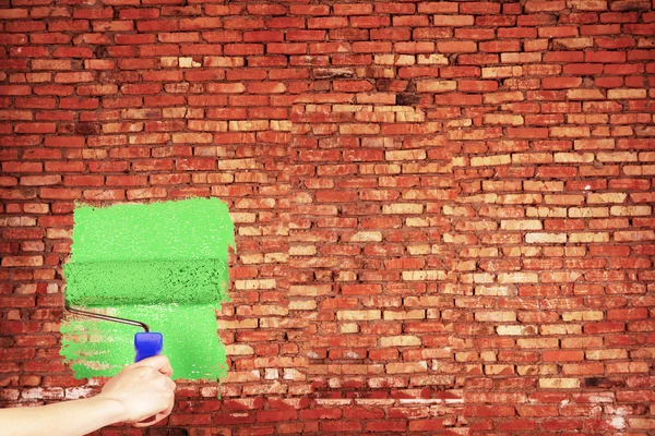 stock image Hand with painting tool on the brick red wall