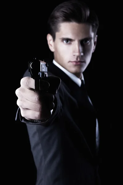 Joven macho atractivo en traje con pistola sobre fondo negro —  Fotos de Stock